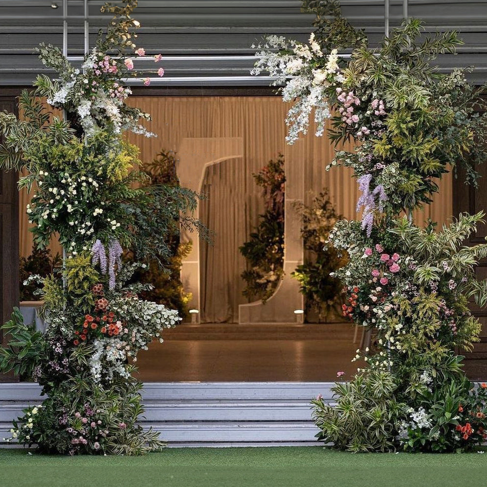 This photo shows an archway of roses, hydrangeas, and other flowers. The Arch is located in a beautiful garden with blue sky and white clouds in the background. The arch is a backdrop decoration for a wedding party and includes a frame. This photo is perfect for a wedding theme search and can also be used to decorate a wedding website or wedding invitations.