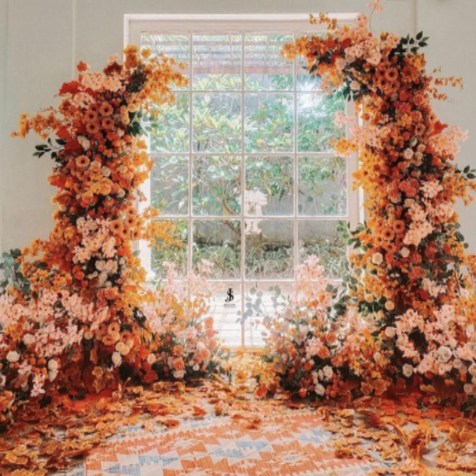 This is a picture of a Leda floral arch decoration for a bridal party backdrop in 2023. Decoration includes a white floral arch decorated with flowers, greenery and ribbons. Arch is located in a beautiful outdoor scene with green trees and blue sky. The decor is the perfect backdrop for a bridal party and is sure to wow your guests.