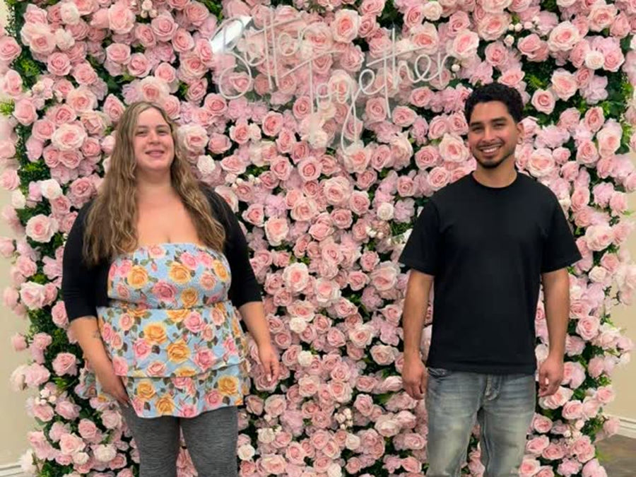 Couple standing in front of a blush pink Rose Morning flower wall
