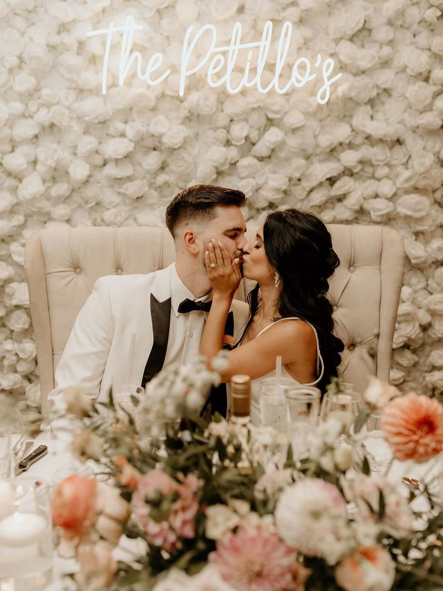Newlyweds seated at their sweetheart table in front of a white flower wall
