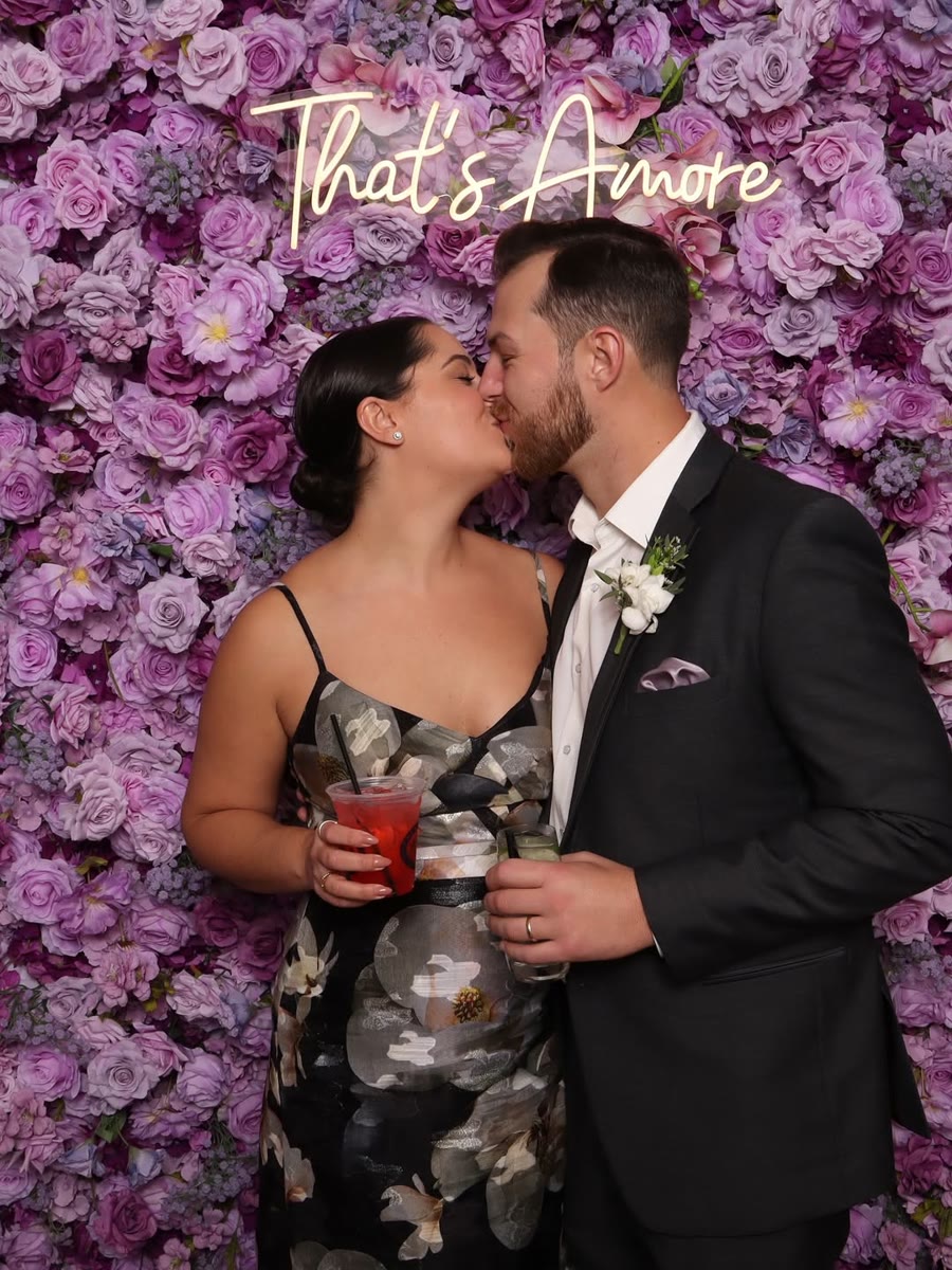 A couple kissing in front of a purple flower wall