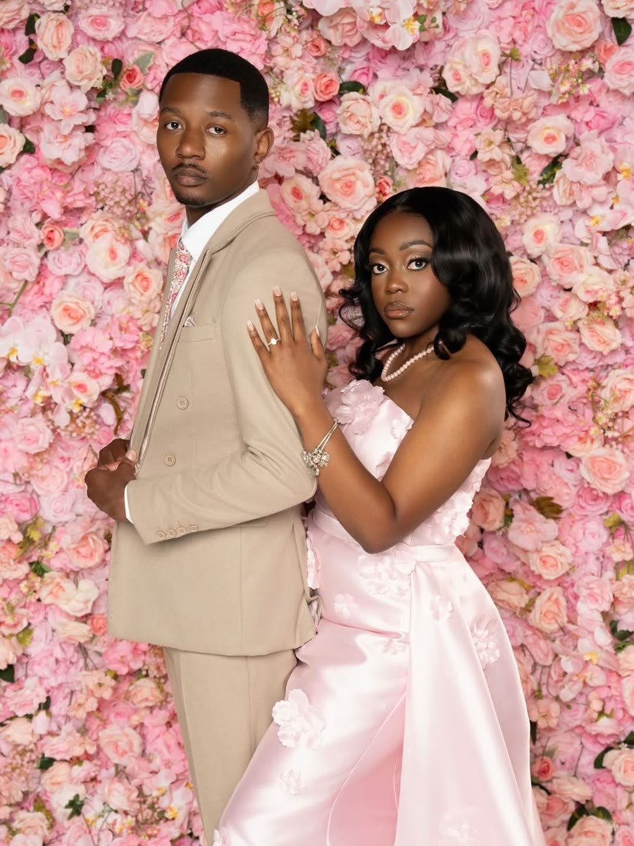 A couple posing in front of a blush pink flower wall