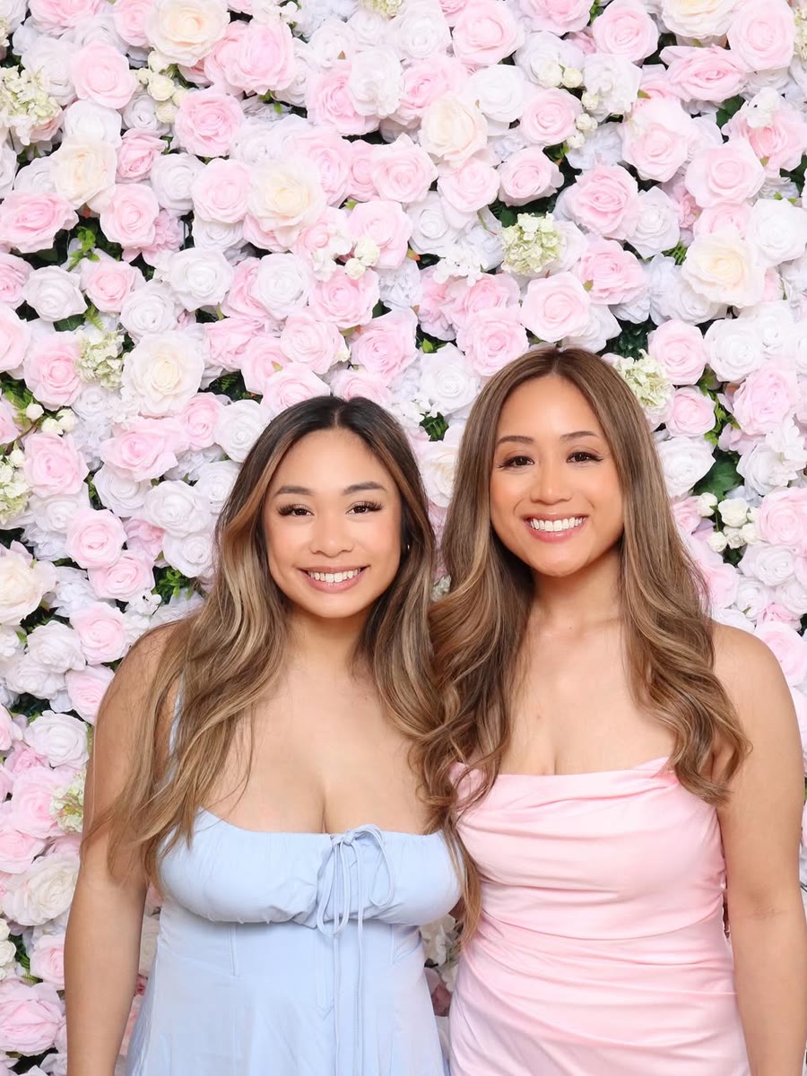 Two guests smiling in front of a pale pink flower wall